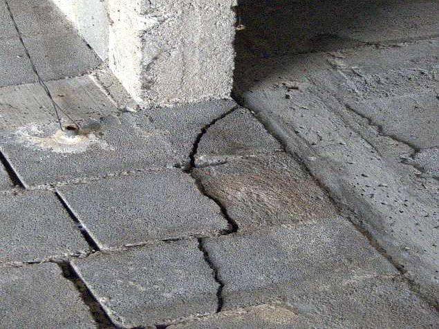 Fissures en escalier dans un mur en blocs béton et dans le dallage au pied d’un poteau