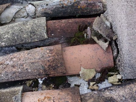 Tuiles cassées et solin dégradé le long d’un mur, en couverture