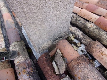 Tuiles brisées et raccord dégradé au pied d’une souche de cheminée