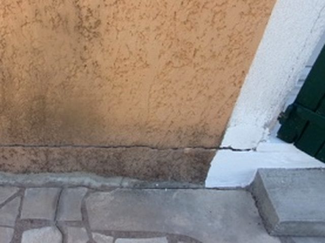 Fissure de l’enduit en pied de façade, à l’angle d’une ouverture